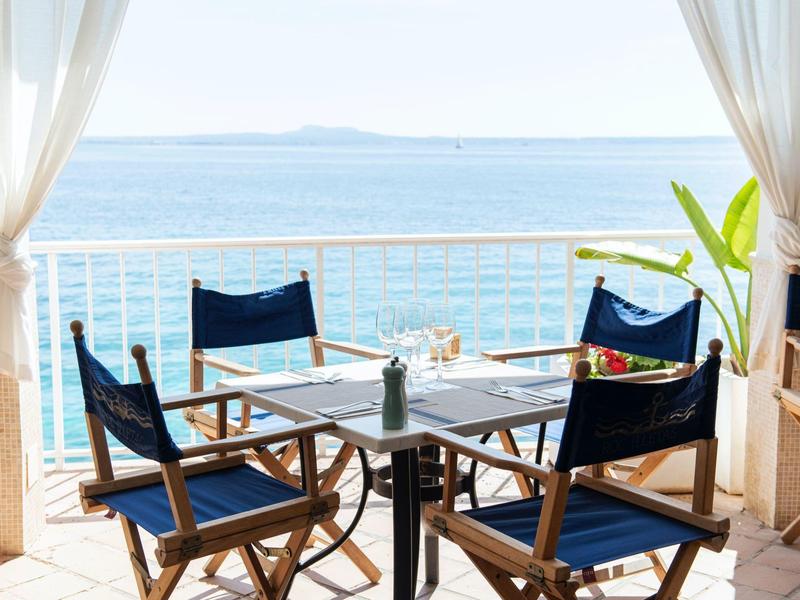 Terrace with table and four chairs overlooking the blue sea under a clear sky.