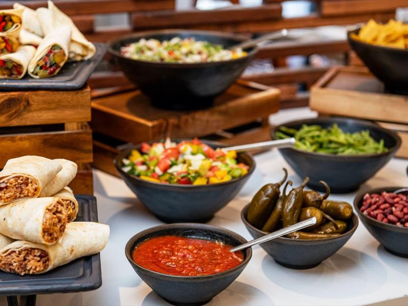 Various bowls with Mexican food like salsa, jalapeños, beans, and wraps on a buffet table