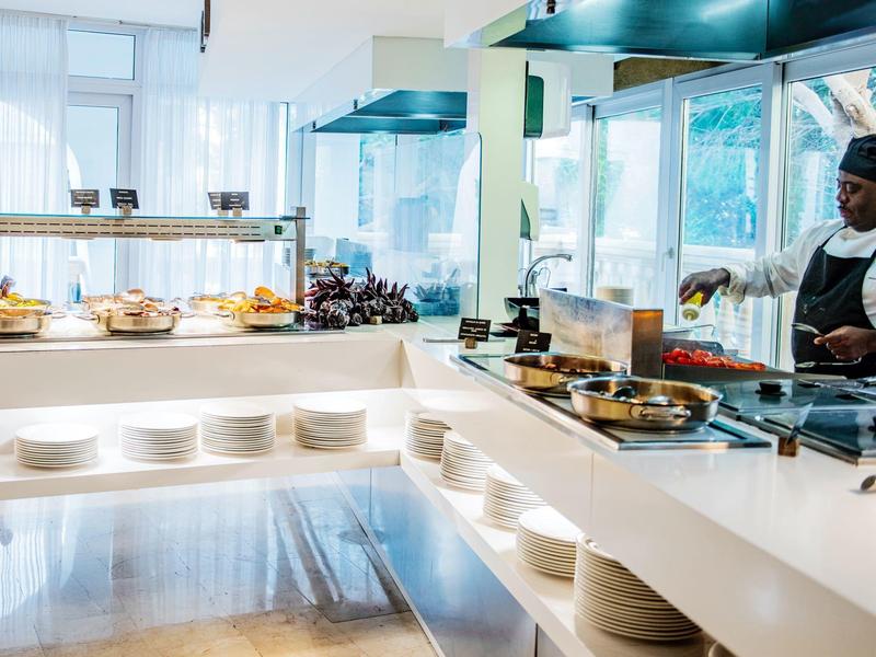 Modern hotel kitchen with open cooking area and buffet, chef preparing food.