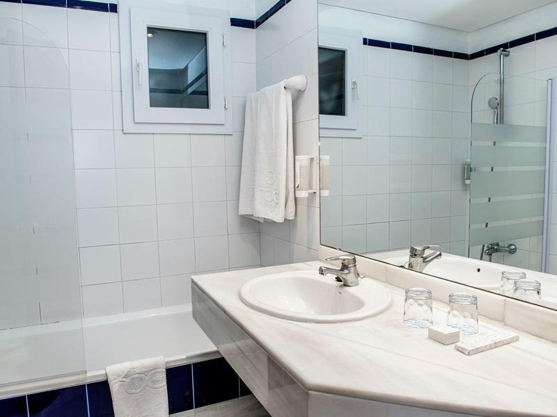 Bright bathroom with sink, mirror, bathtub, and white towels hanging on the wall.