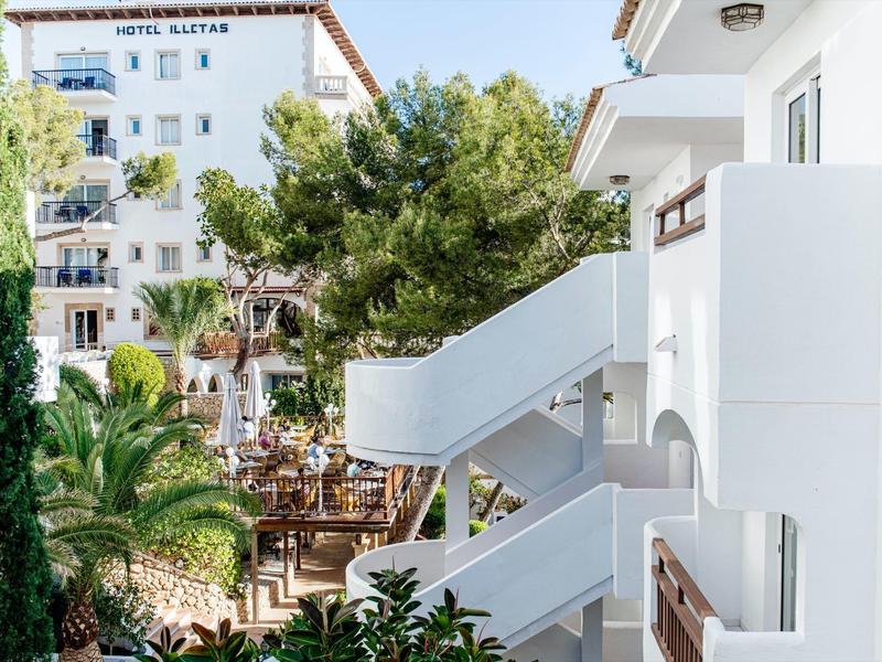 View of a white hotel with an outdoor staircase and green trees in a sunny setting.
