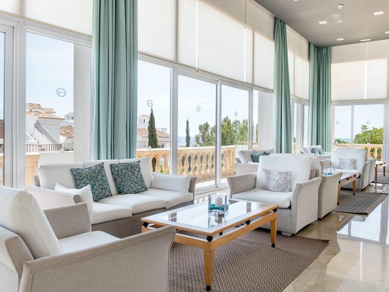 Bright, modern lounge area with large windows, white sofas, and a view of a terrace.