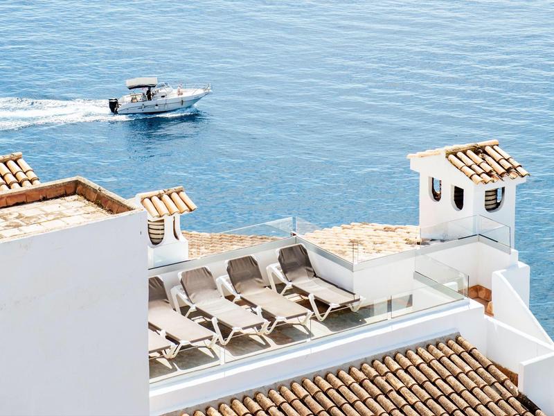 White terrace with sun loungers overlooking the sea with a boat in the background.