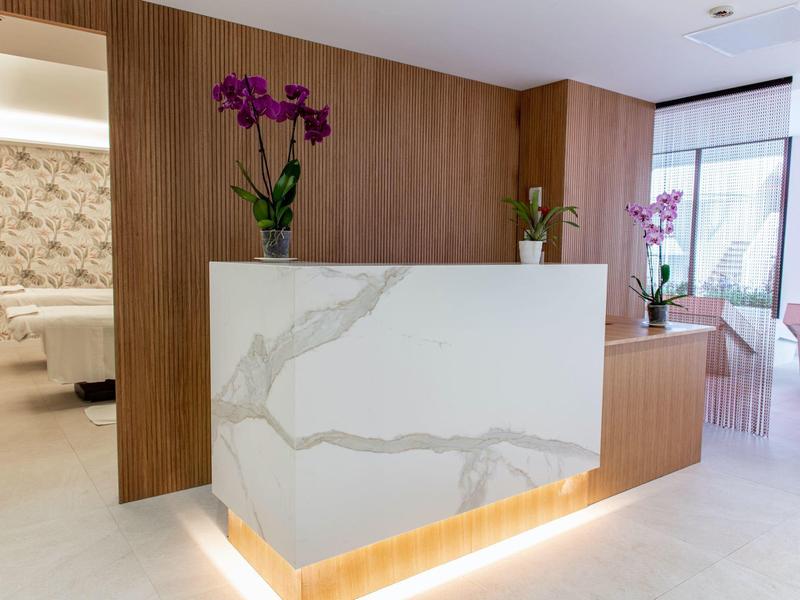 Modern reception area with white marble counter and wood paneling, decorated with orchids.
