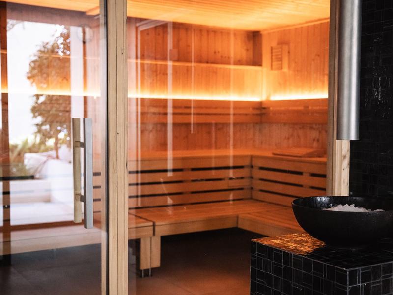 Modern sauna with wooden benches and indirect lighting next to a black sink.