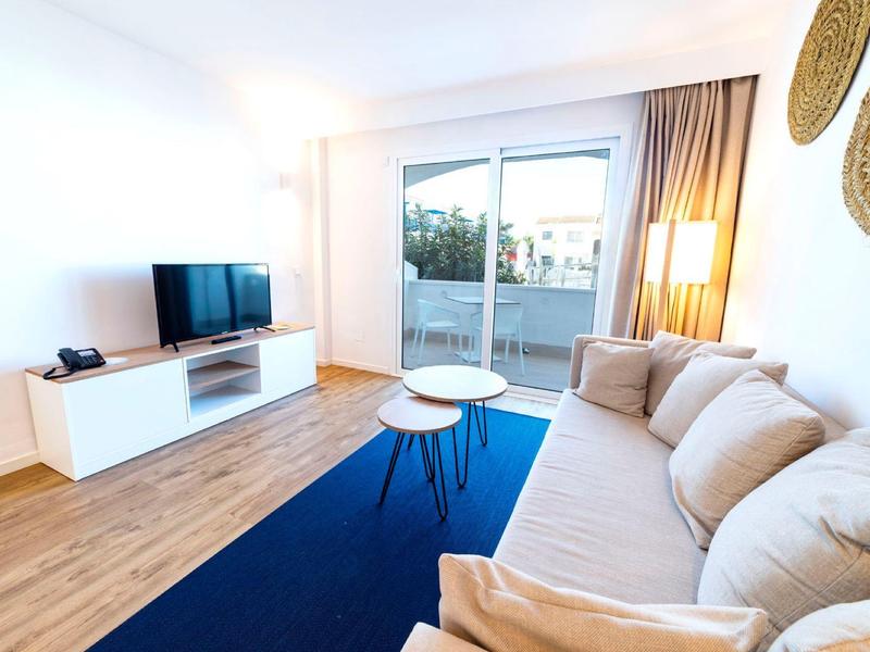 Helles Wohnzimmer mit cremefarbener Couch, blauem Teppich, weißem TV-Schrank und Holzboden.