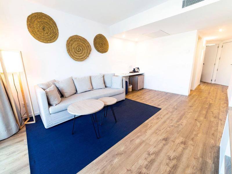 Heller Wohnraum mit grauer Couch, blauer Teppich, drei runden Wanddekorationen und Holzfußboden.