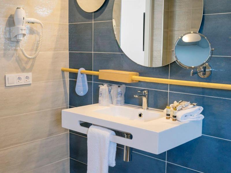 Moderne Badezimmerwand mit blauen Fliesen, rundem Spiegel und weißem Waschbecken mit Handtuch.