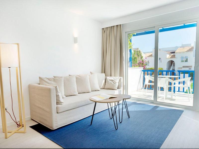 Helles Wohnzimmer mit weißem Sofa, kleinem Tisch, blauem Teppich und großer Glas-Schiebetür.