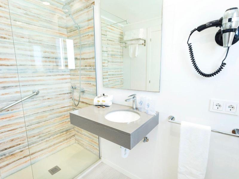 Modernes Badezimmer mit Glasdusche, Spiegel, Waschbecken, Handtuchhalter und Haartrockner an weißer Wand.