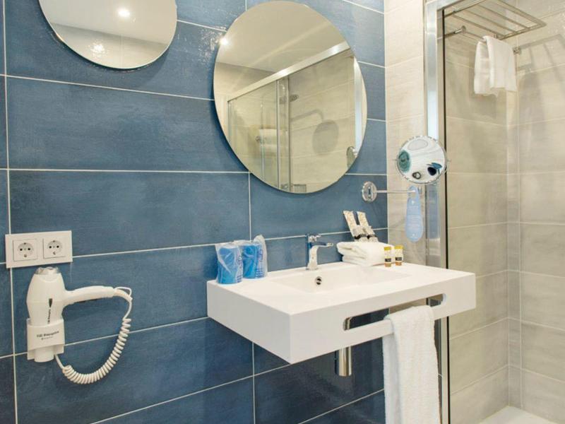 Modernes Badezimmer mit blauen Wandfliesen, zwei runden Spiegeln, Waschbecken und Glastür-Dusche.
