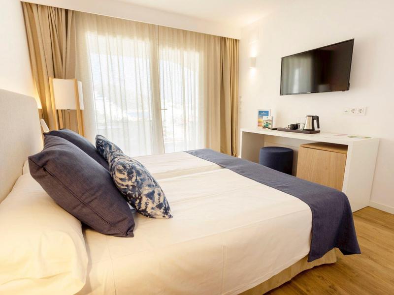 Modernes Schlafzimmer mit Doppelbett, weißen und blauen Kissen, Holzboden und Wand-TV.