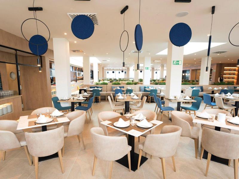 Moderner Restaurantinnenraum mit weißen Stühlen, runden Tischen und blauen, hängenden Dekorationen.