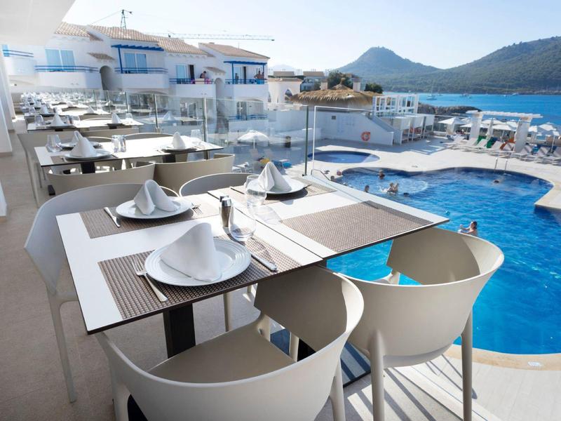 Moderner Außenbereich mit Pool, weißen Stühlen, gedeckten Tischen und blauem Himmel.