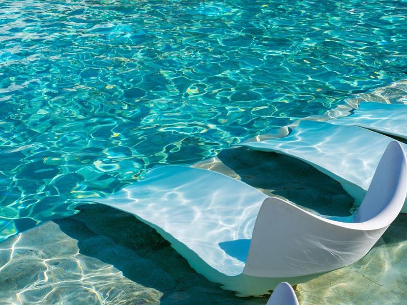 Ein weißer Liegestuhl steht teils im klaren, türkisfarbenen Wasser eines Pools.