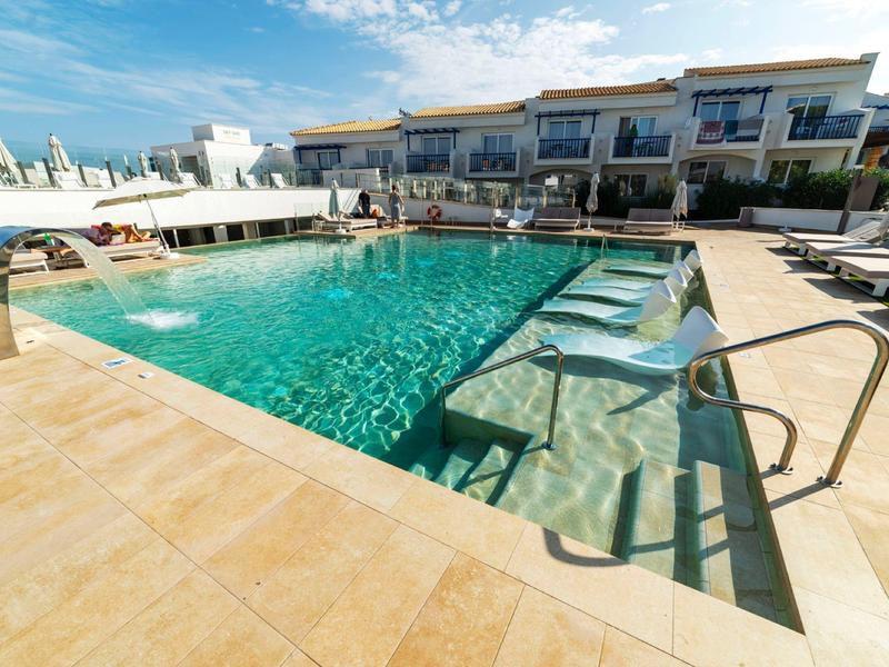 Großer Außenpool mit klar blauem Wasser und Sonnenliegen vor modernen Apartments.