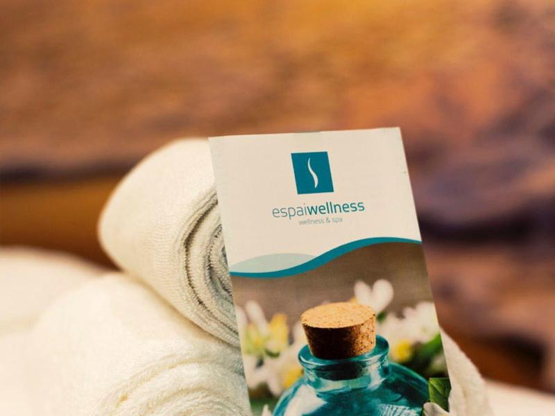 Zwei weiße Handtücher, eine Karte mit blauer Flasche und weißen Blüten, unscharfer Hintergrund.