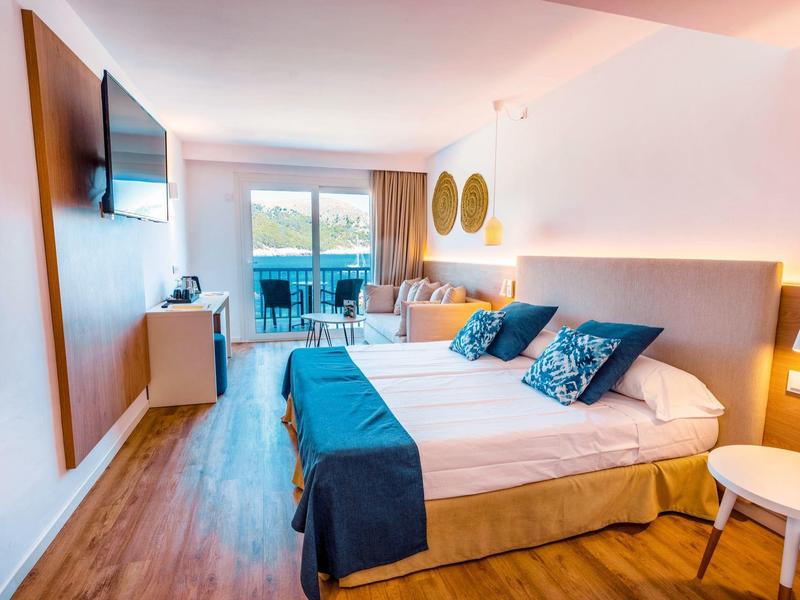 Modernes Hotelzimmer mit Doppelbett, hellen Holzböden, Fernseher und Balkon mit Außenblick.