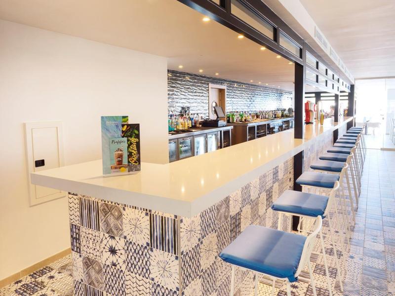 Moderner Barbereich mit gemusterten Fliesen und blauen Hockern in einem hellen Raum.