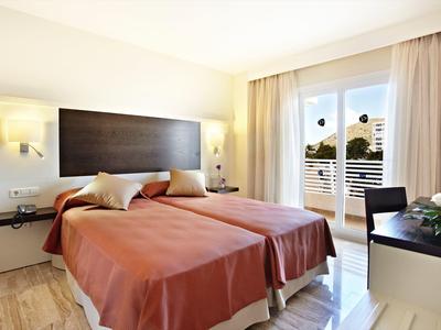 Helles Schlafzimmer mit zwei Einzelbetten, braunen Decken, großem Fenster und modernen Möbeln.