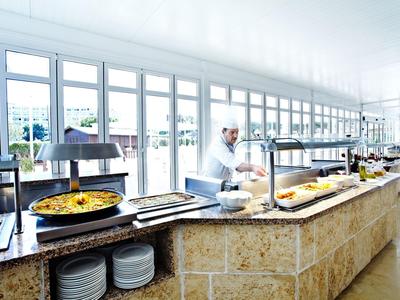 Ein heller Buffetbereich mit großen Fenstern, mehreren Schüsseln und einem Koch hinter der Theke.