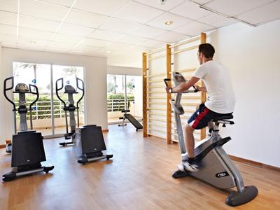 Mann trainiert auf einem Heimtrainer in einem hellen Fitnessraum mit mehreren Geräten.