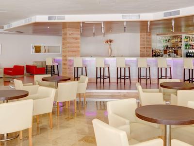 Helle Café-Lounge mit Holztheke, runden Tischen und weißen Polstersesseln in modernem Design.