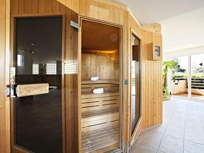 Holzsauna mit Glastür in hellem, modernem Raum und Zugang zu Balkon mit Pflanzen.