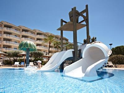 Wasserrutsche in blauem Pool mit Hotel und Palmen im Hintergrund bei klarem Himmel.