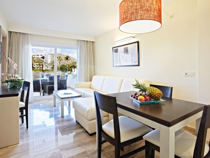 Heller Wohn- und Essbereich mit beigem Sofa, dunklem Holztisch, Stühlen und Balkon mit Glasfenstern.