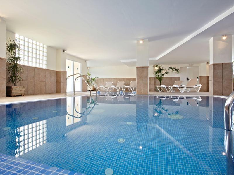 Heller Innenpool mit hellblauen Fliesen, Stühlen, Tischen und großen Fenstern.