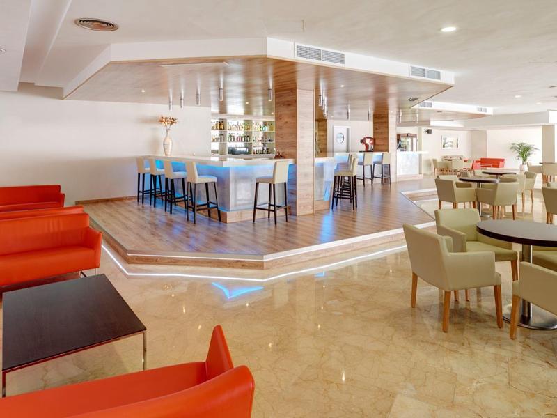 Heller Lounge-Bereich mit roten Sofas, beigen Sesseln und Holzakzenten auf hellem Boden.