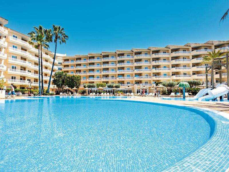 Großer Außenpool mit blauer Wasserfläche vor mehrstöckigem Hotel unter klarem Himmel.