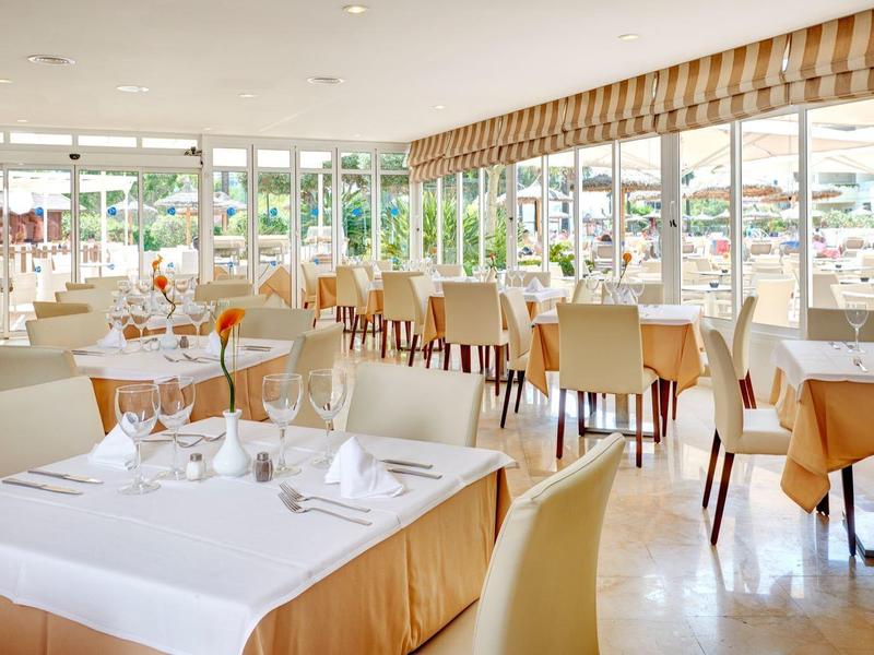 Helles Restaurant mit großen Fenstern, gedeckten Tischen und cremefarbenen Stühlen in hellem Ambiente.