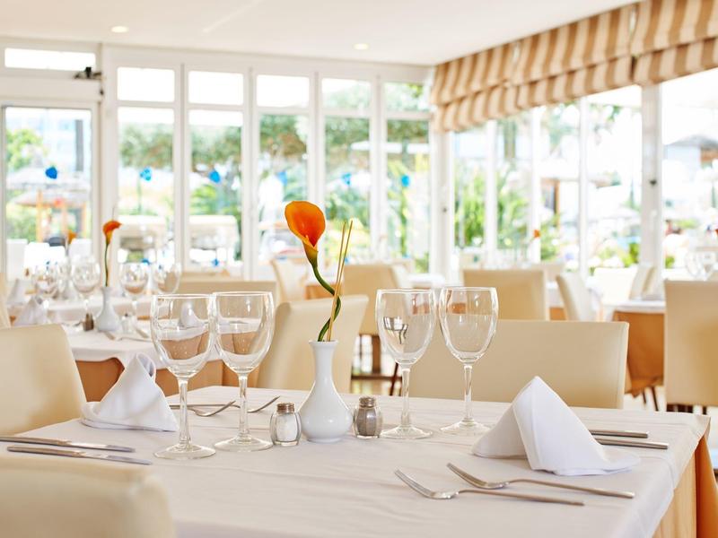 Elegantes Restaurant mit weiß gedeckten Tischen, Glasgeschirr und orangefarbenen Blumen als Dekor.