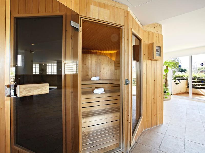 Holzsauna mit Glastür in hellem, modernem Raum und Zugang zu Balkon mit Pflanzen.