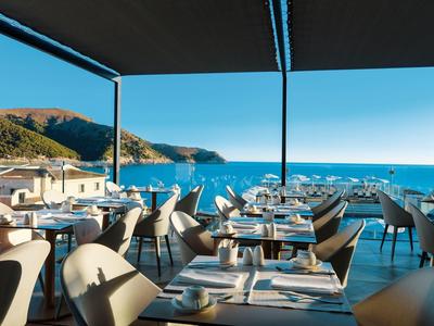 Open-air restaurant with set tables and sea view under clear sky.