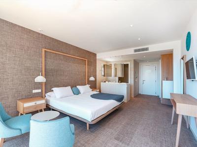 Modern hotel room with large bed, seating area, and desk in neutral tones.