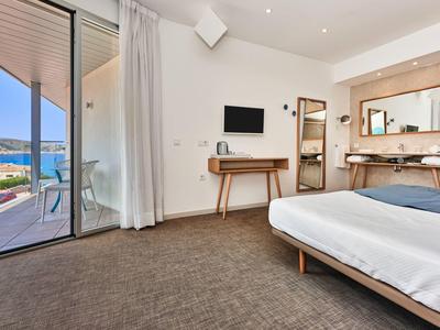 Modern hotel room with double bed, desk, TV, and balcony overlooking the sea.