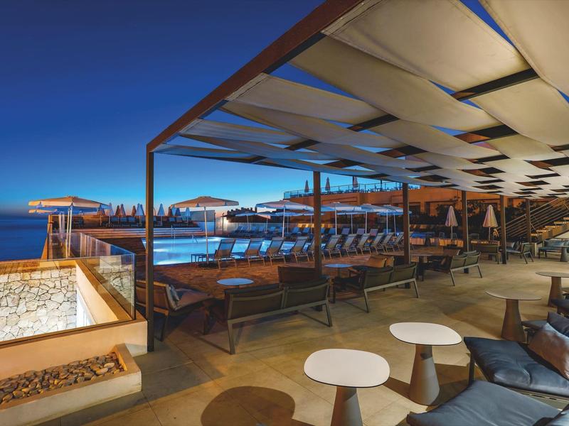 Modern outdoor area with covered seating and sea view at dusk.