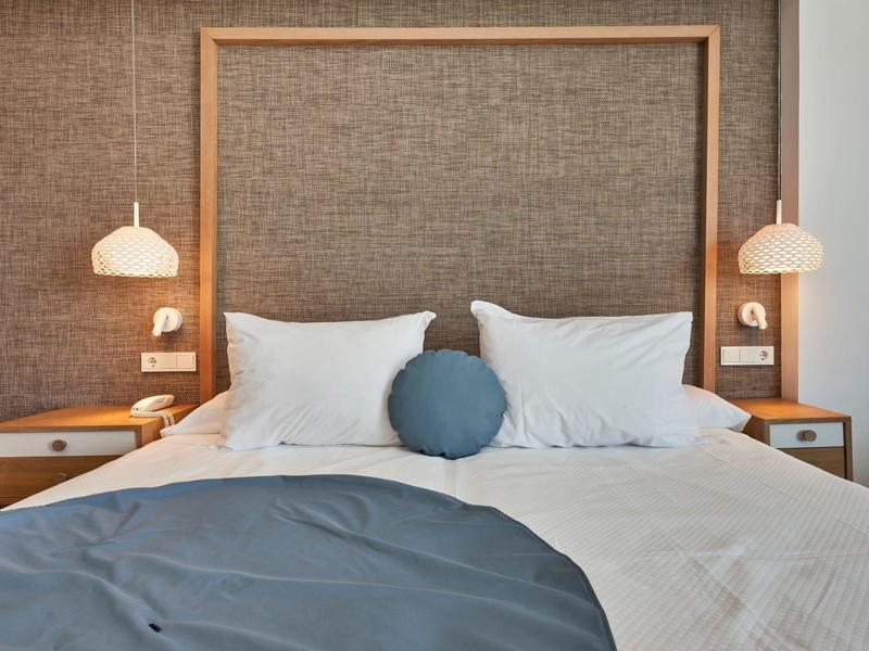 Modern hotel room with double bed, white and blue bedding, and hanging bedside lamps
