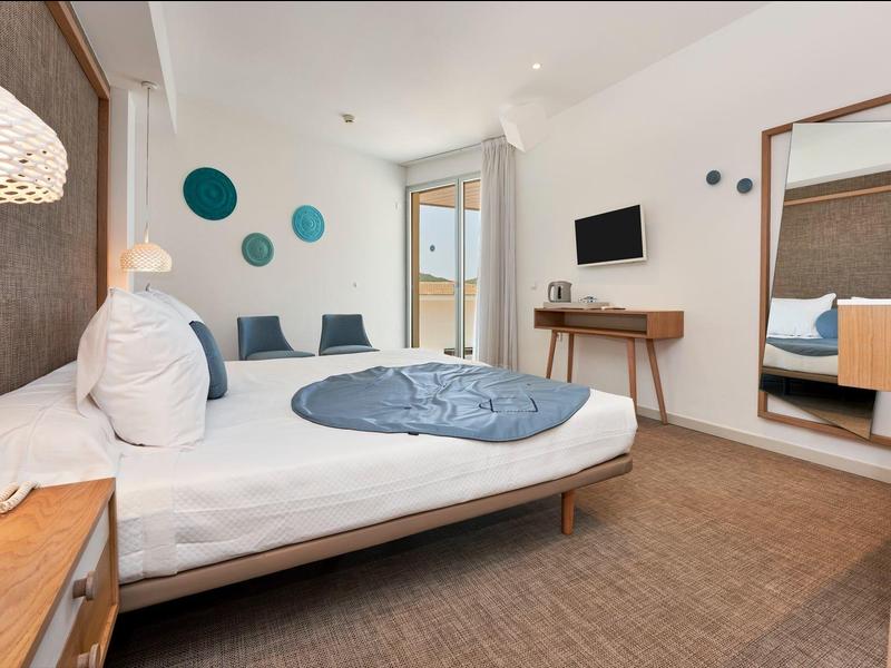 Modern hotel room with double bed, seating area, large mirror, and balcony.