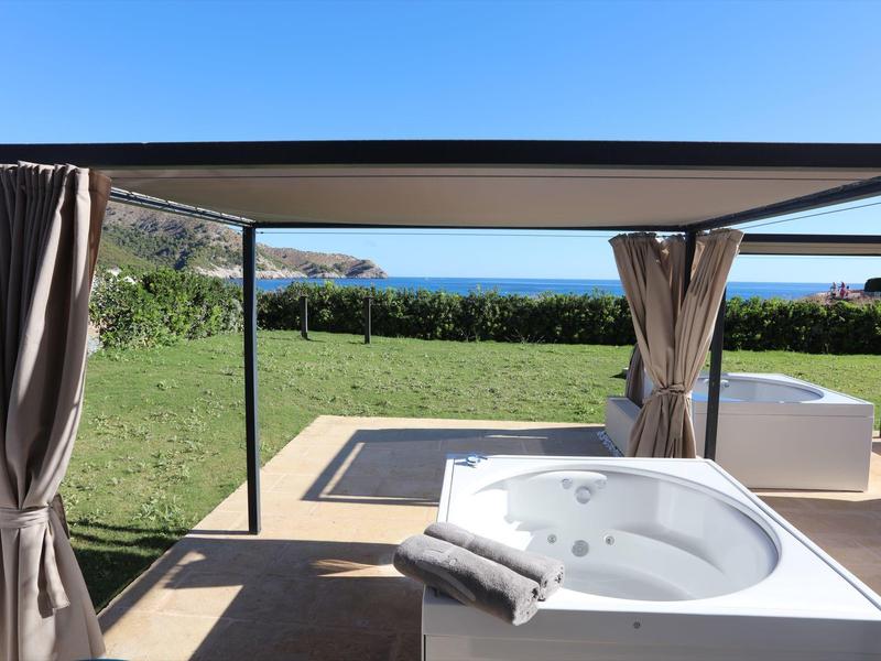 Outdoor jacuzzi with curtains overlooking manicured garden and sea in the background