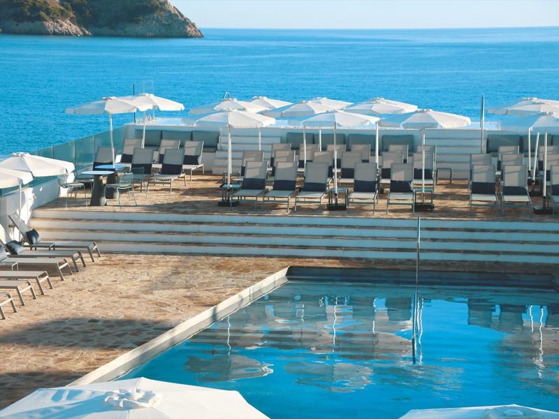 Pool area with sun loungers and white umbrellas next to calm sea.