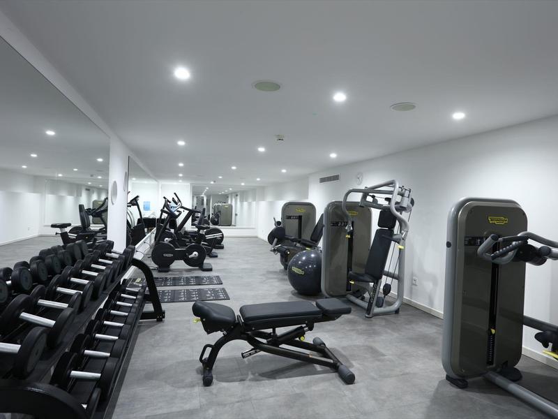Modern gym with dumbbells, workout machines, and bench, white painted walls.