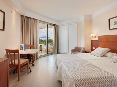 Bright hotel room with two single beds, desk, and balcony access with a view.