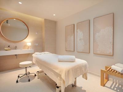 Bright spa room with treatment table, round mirror, and soft lighting.