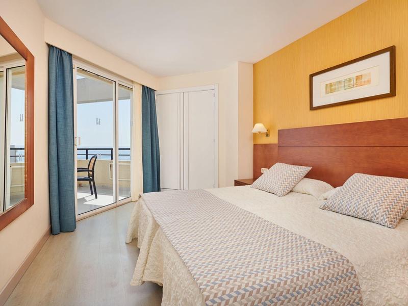 Bright hotel room with double bed, balcony access, and sea view.