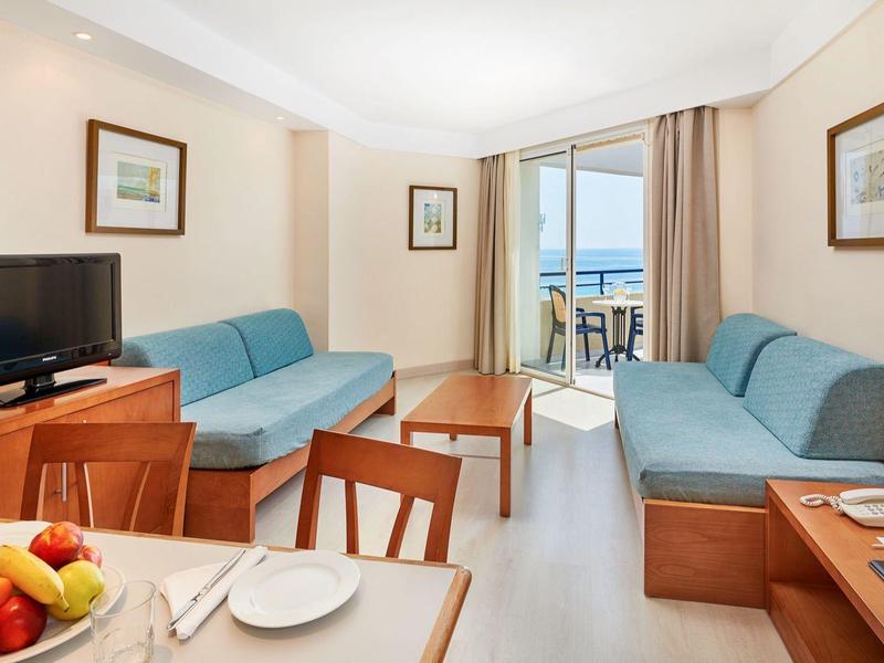 Bright living room with two blue sofas, TV, and dining table with fruit bowl.