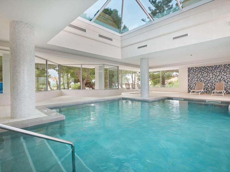 Bright indoor pool with large windows and a glass roof in a hotel.